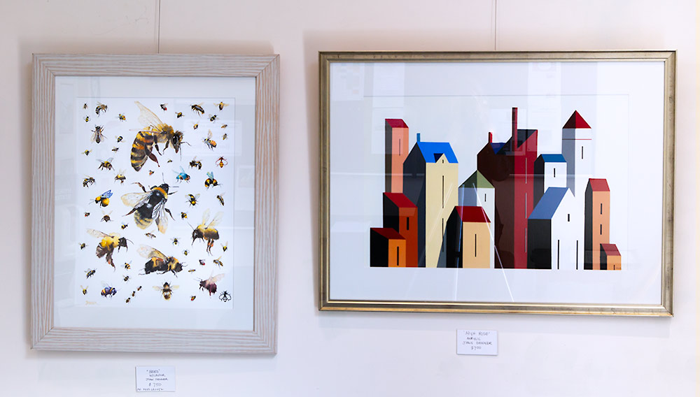 Artworks by Joan Denner Framed artworks by Joan Denner, one of bees in watercolour and one of stylized buildings in bright colours.