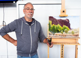Ben Winspear with completed demo painting of a landscape with rocky hill and trees in foreground.