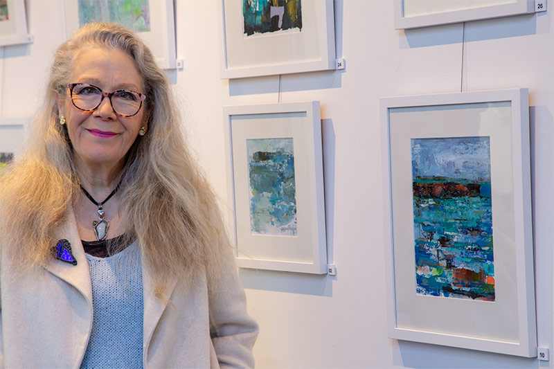 Su Fishpool - Colour My World Exhibiton. Photo of the artist with artworks in the background.